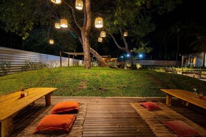 An outdoor dining area with wooden tables and benches, surrounded by a grassy lawn and trees. - Cond em Resort Pe na Areia - By MME (Maceió)