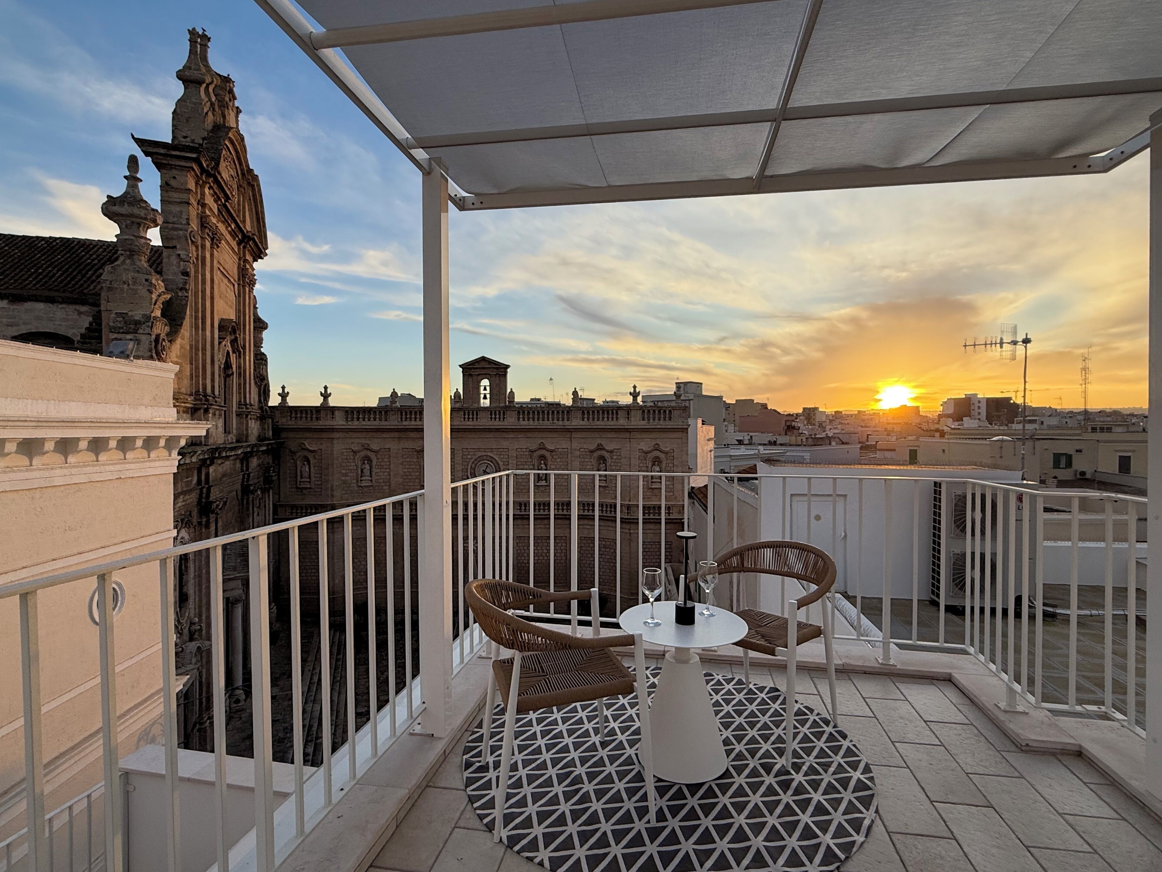 Un balcón con mesa y sillas, con vistas a un edificio histórico y un atardecer.