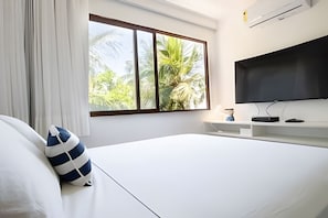 Ein Hotelzimmer mit Bett, Fernseher, Fenster mit Blick auf Bäume und einer weißen Wand.