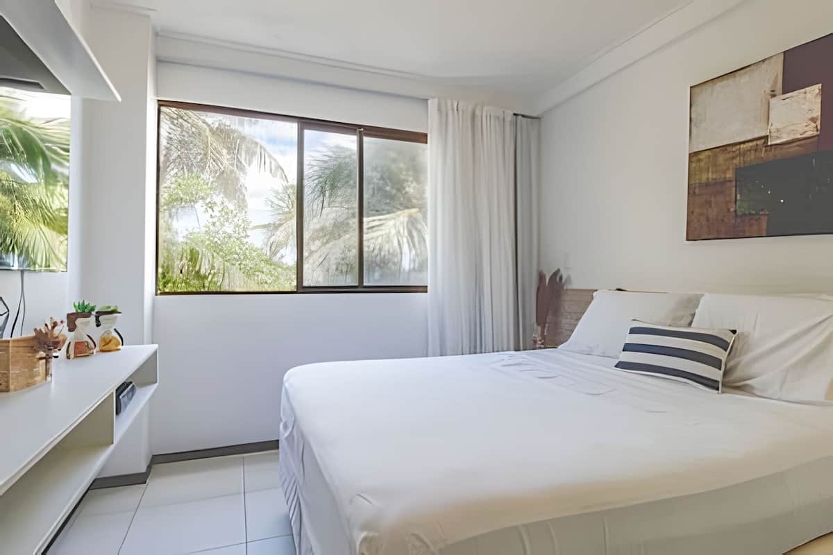 A bedroom with a bed, a desk, and a large window with curtains.