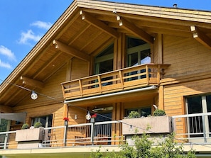 A wooden building with a balcony, large windows, and outdoor seating.