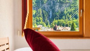 Ein Bett mit einem roten Kopfkissen und einem Fenster mit Blick auf eine gebirgige Landschaft.