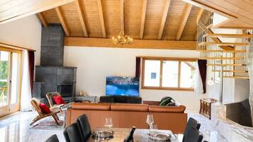 Een ruime eetruimte met een hoog houten plafond, een open haard en een televisie op de achtergrond.