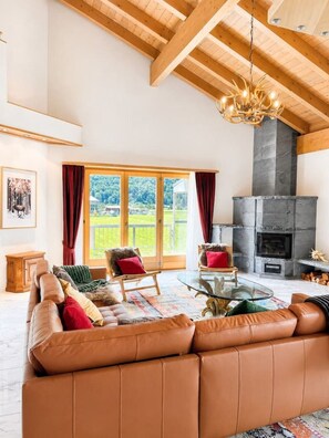 A spacious living room with a large leather sofa, two armchairs, a glass coffee table, and a fireplace.