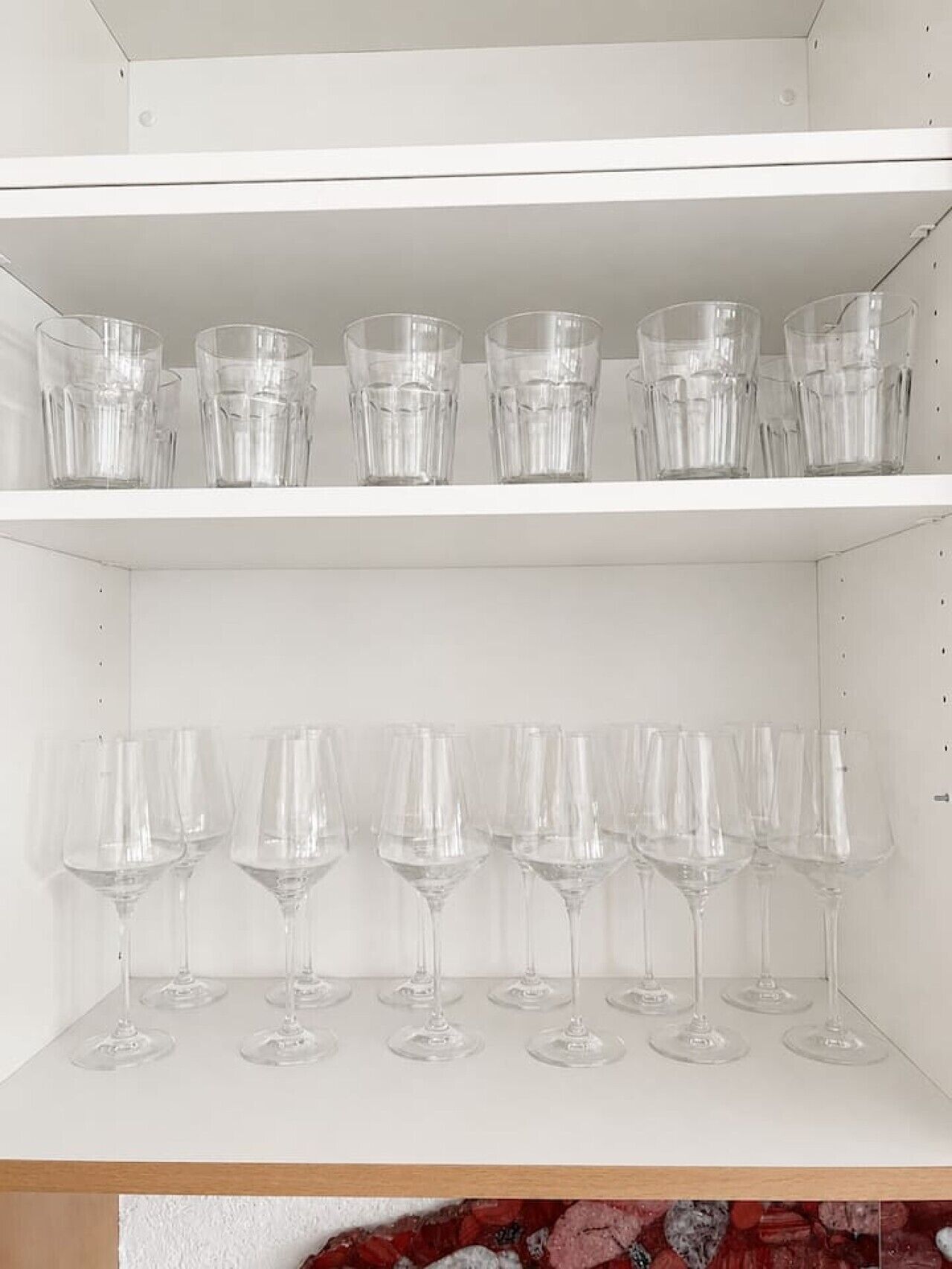 A white shelf with multiple clear glasses and wine glasses.
