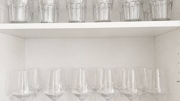 A white shelf with multiple clear glasses and wine glasses.