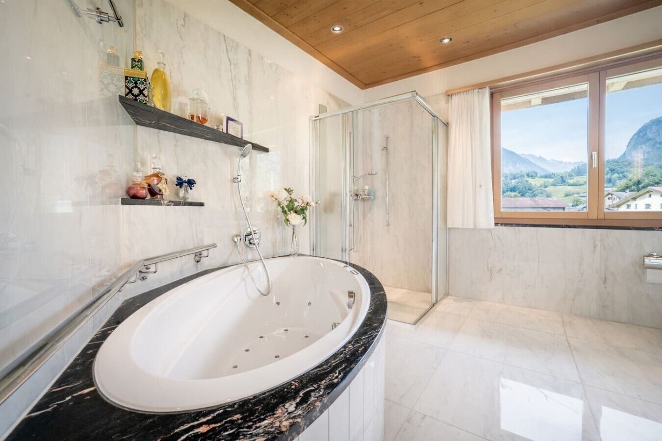 A bathroom with a large bathtub, a glass shower enclosure, and a view of the mountains through a window.