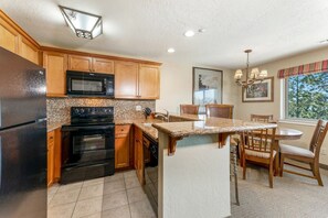 A kitchen with wooden cabinets, a black refrigerator, a microwave, an oven, a granite countertop, a sink, and a dining area with chairs and a table. - Serene 2-bedroom condo in Stateline perfect for your getaway (Stateline)