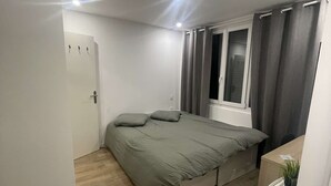 Quarto com cama, mesa de cabeceira, janela com cortinas e porta.