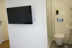 Et badeværelse med toilet, bruser og et ophængt fjernsyn.