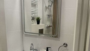 Um banheiro com pia branca, espelho, porta-toalhas e chuveiro.