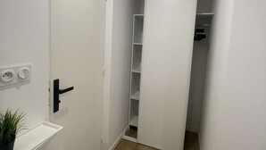 Um corredor com uma porta branca, uma pequena planta e uma estante branca.