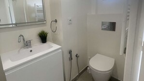 Casa de banho com lavatório branco, espelho e sanita.