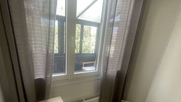 A room with a wooden desk, a chair, a radiator, a window with curtains, and a trash bin.