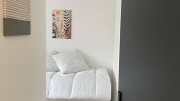 A bedroom with a bed, a white bedside table, a wall with two artworks, and a door.