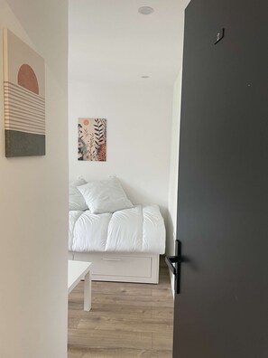Et soveværelse med en seng, et hvidt natbord, en væg med to kunstværker, og en dør.