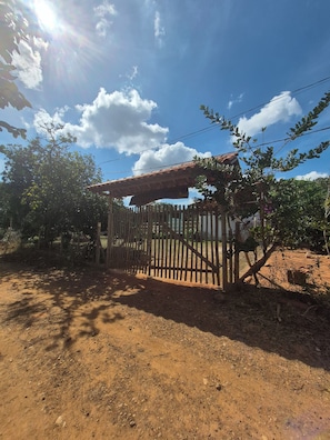 A rustic wooden gate with a corrugated metal roof, surrounded by trees and a dirt path.