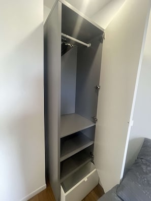 Een inloopkast met een metalen stang, een schuifdeur en een klein lade.