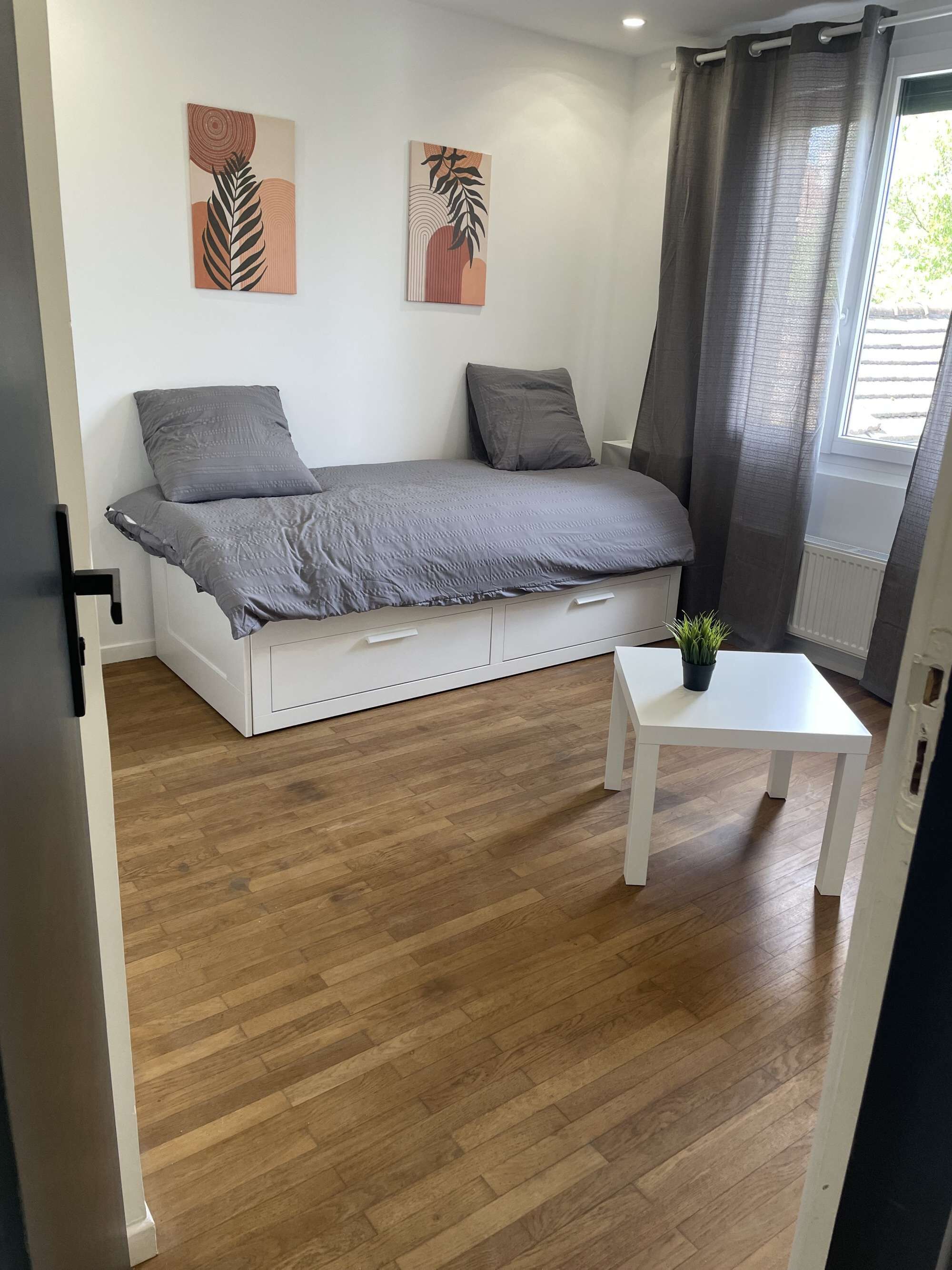 Een moderne slaapkamer met een bed, een tafeltje en twee kunstwerken aan de muur.
