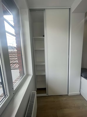 Een kamer met een raam, een radiator en een witte kast met meerdere planken.