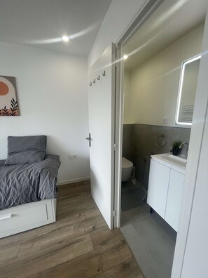 A bedroom with a bed, a bathroom with a toilet and sink, and a door leading to another room. - Cozy Private Room | Coliving 30min from Paris St-Lazare (Argenteuil)
