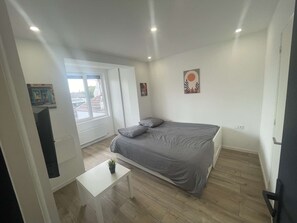 A bedroom with a bed, a small table, a window, and a wall with a picture. - Cozy Private Room | Coliving 30min from Paris St-Lazare (Argenteuil)