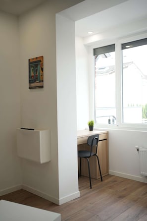 Een kamer met een bureau, stoel, radiator en een raam met uitzicht.