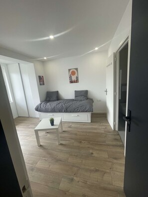 Et soveværelse med en seng, et lille bord med en plante, et billede på væggen og en dør.