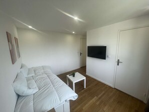 Moderni, pelkistetty huone, jossa on valkoinen sohva, pieni valkoinen pöytä, seinälle asennettu litteänäyttöinen televisio ja puulattia.