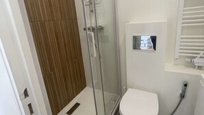 Moderni kylpyhuone, jossa on lasinen suihkuseinä, valkoinen wc-istuin ja peilillä varustettu, seinään upotettu pesuallas.