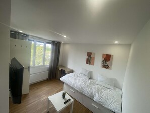 Een moderne slaapkamer met een bed, een klein wit tafeltje, een televisie en kunst aan de muur.