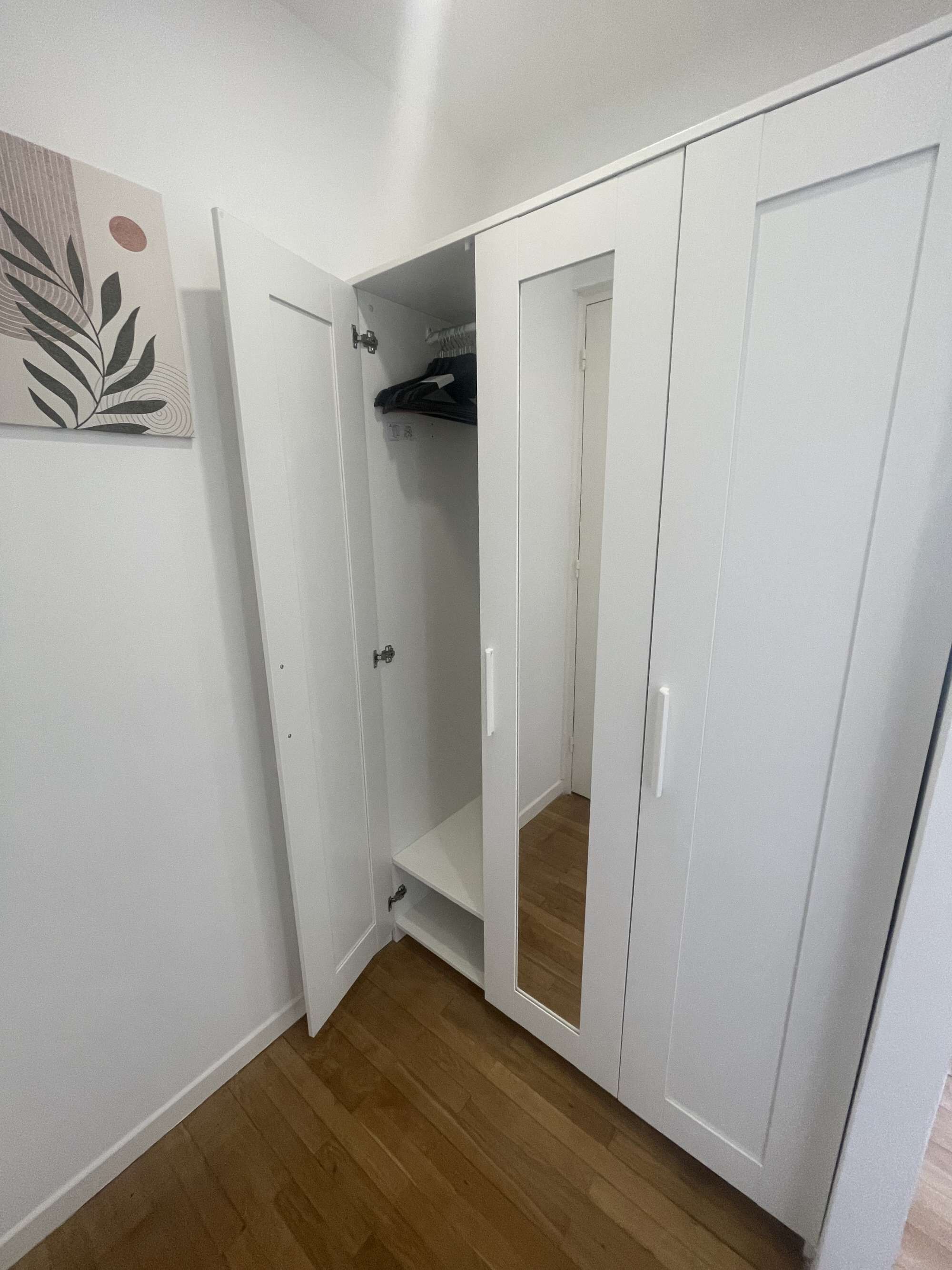 A room with a white wardrobe, a door leading to a closet, and a wooden floor.