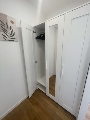 Een kamer met een witte garderobe, een deur naar een inloopkast, en een houten vloer.
