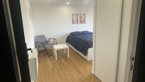 A bedroom with a bed, a small table, a chair, and two wall-mounted artworks. - Cozy Private Room | Coliving 30min from Paris St-Lazare (Argenteuil)
