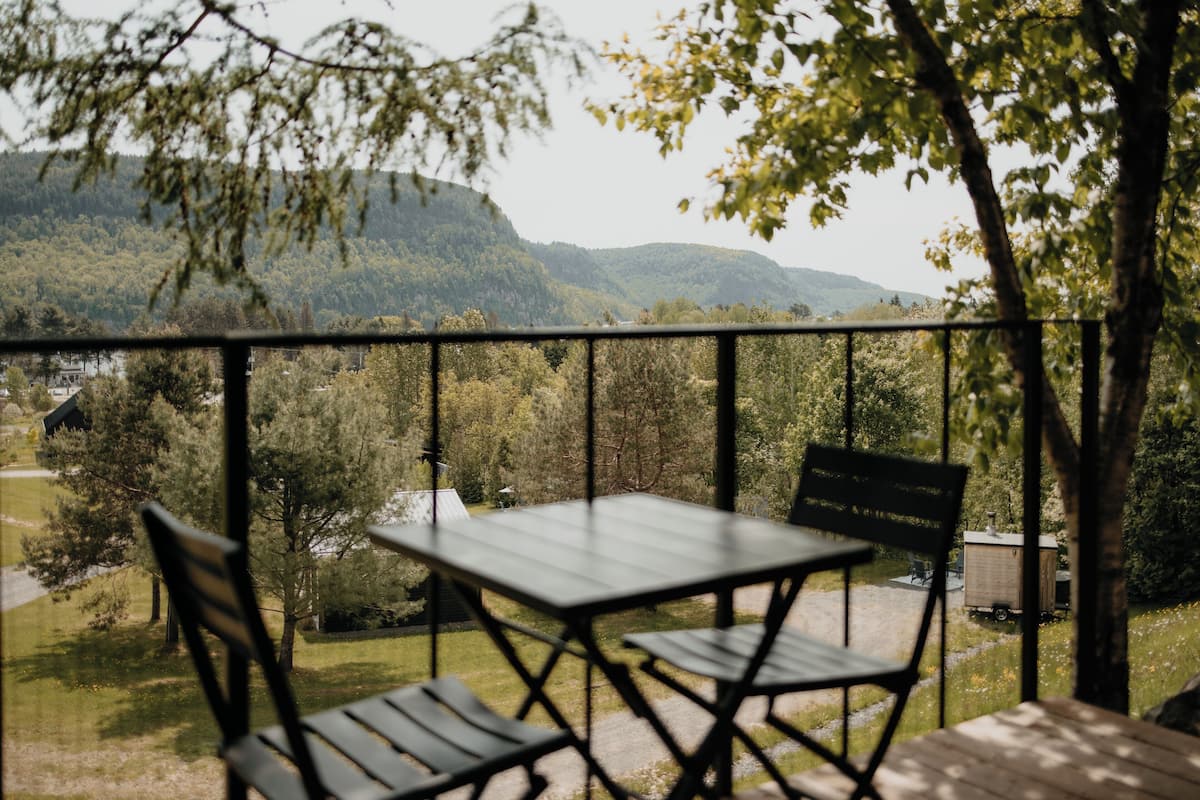A balcony with a table and chairs, overlooking a forested area and mountains.