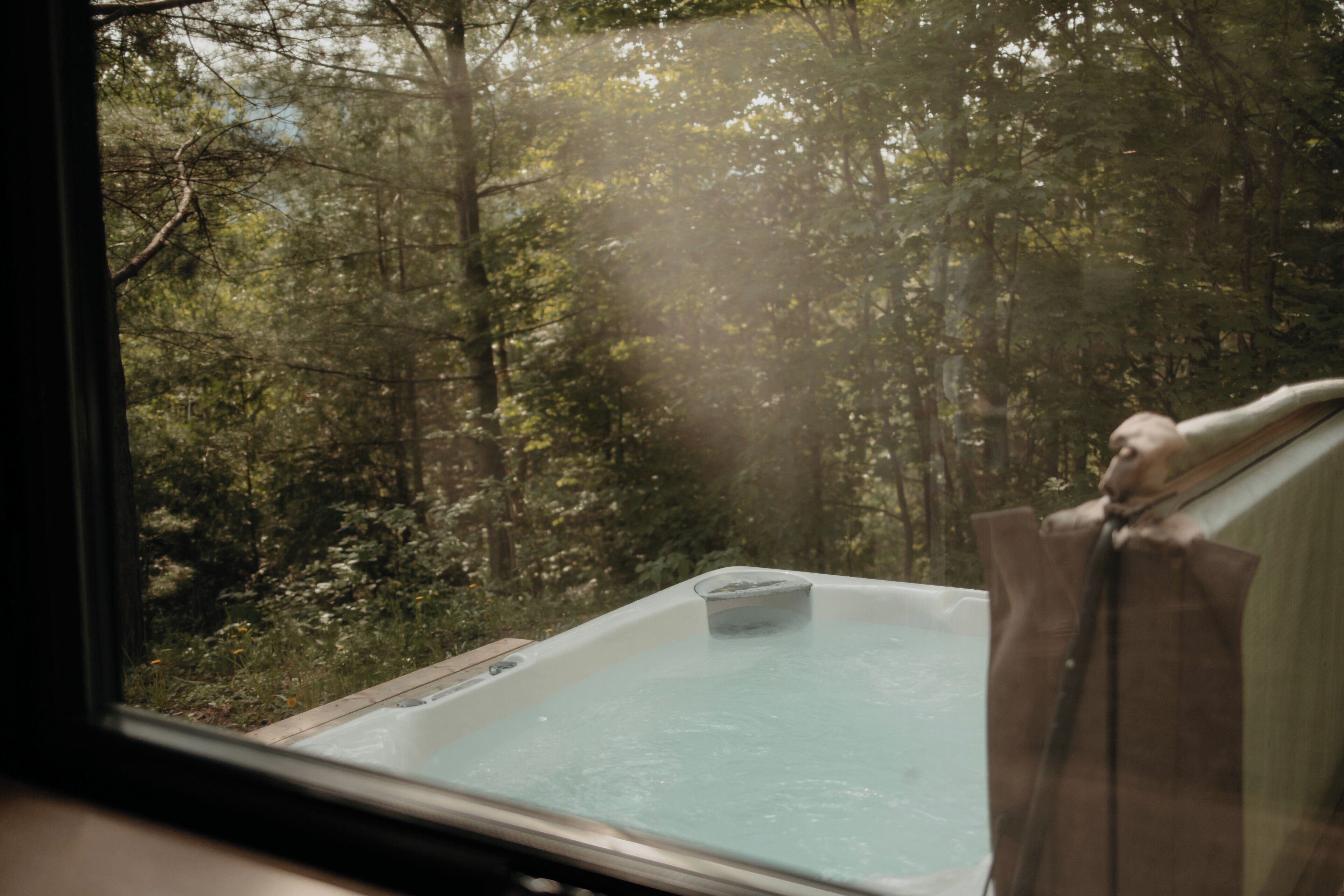 A hot tub with a view of a forest through a window.