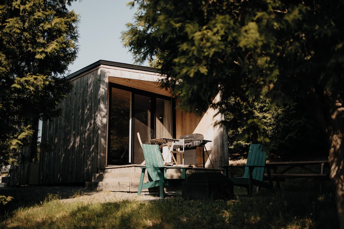 A wooden cabin with a sliding glass door, a grill, and two green chairs.