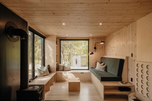 Interior acogedor de una cabaña con un banco incorporado, una mesa pequeña y una ventana con vistas a árboles.