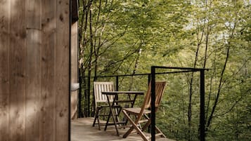 A wooden deck with two chairs and a table, surrounded by dense forest.