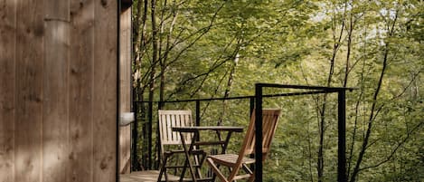 A wooden deck with two chairs and a table, surrounded by dense forest.