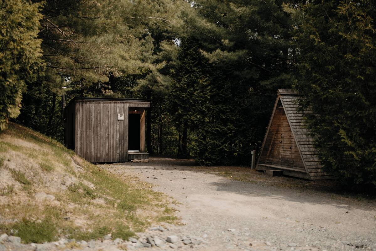 A wooden cabin with a door and a small porch, surrounded by dense forest.