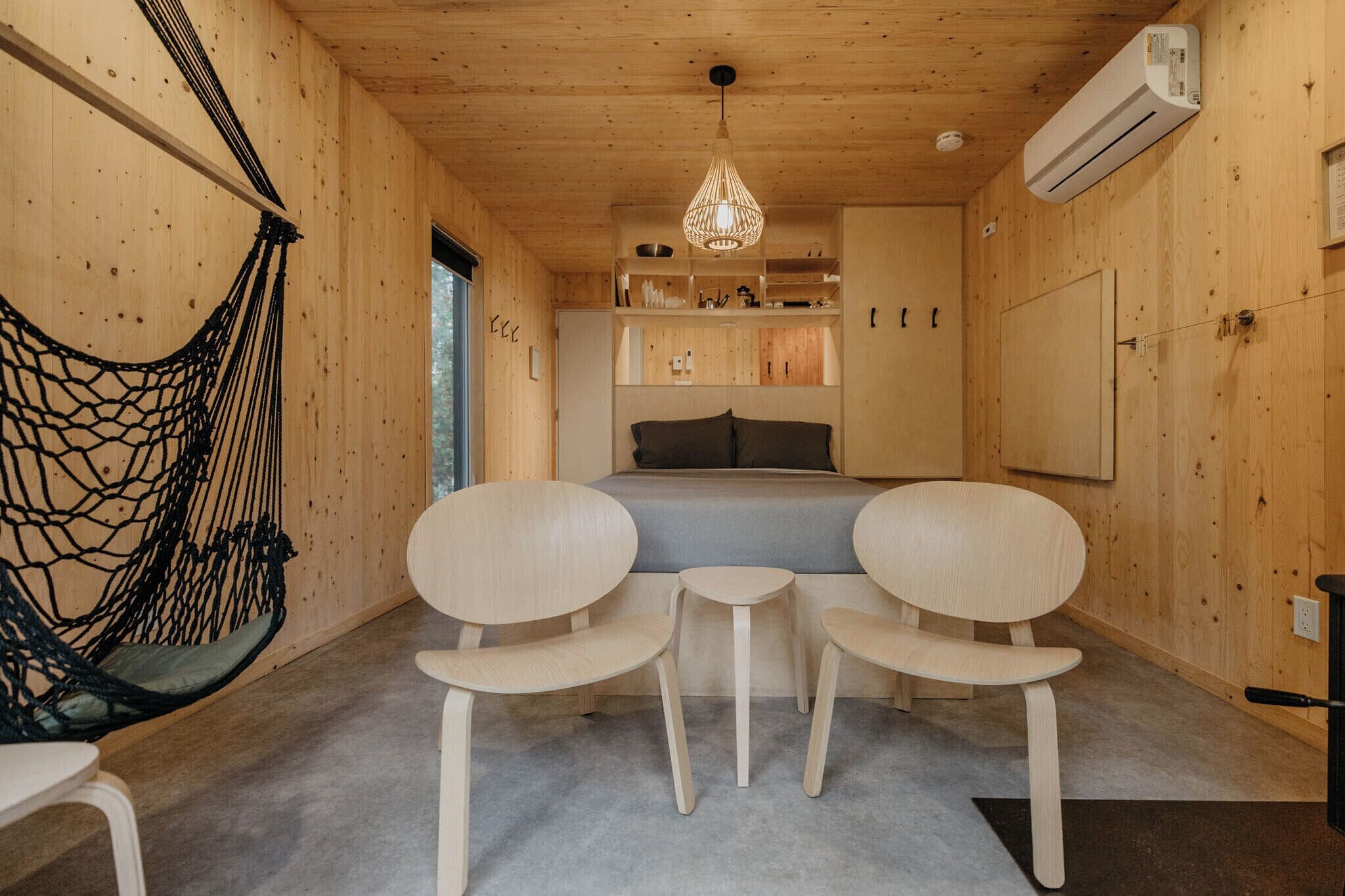 Ein Zimmer mit Holzboden, einem Bett, zwei Stühlen, einer Hängelampe und einer Hängematte.