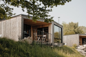 A modern wooden cabin with a glass extension, outdoor seating, and a natural setting.