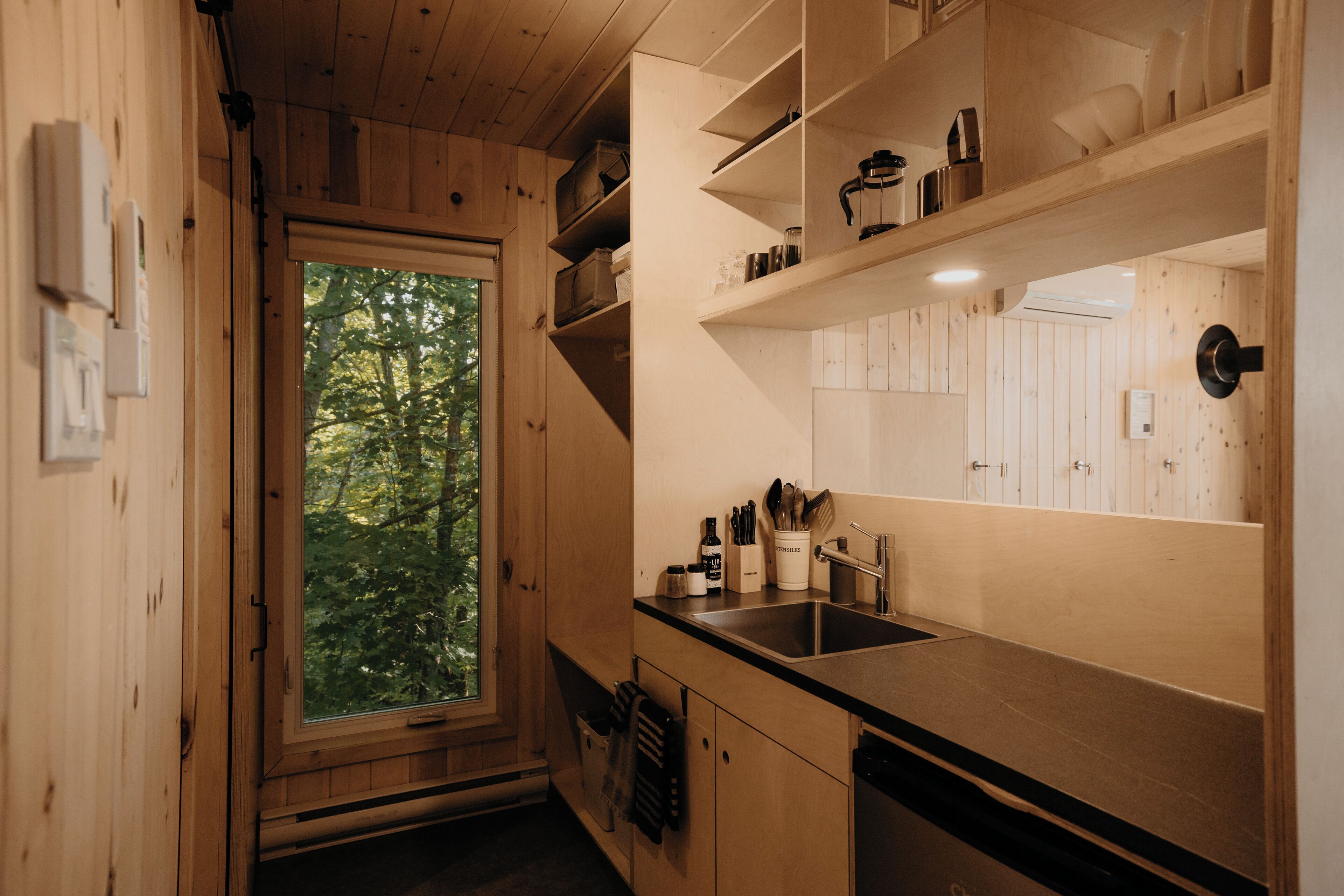 Un intérieur en bois avec une fenêtre, un évier et des étagères remplies d’ustensiles de cuisine.