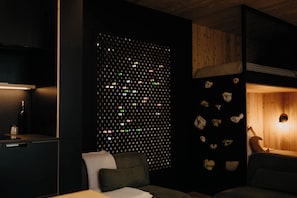 A room with a dark wall featuring a grid of small, colorful lights, a wooden ceiling, a bed with a headboard, and a small table with a lamp. - Nature Nature  (Saint-Jean-Des-Piles)