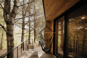 A wooden staircase leading to a room with large windows, a hammock, and a chair outside.
