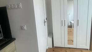 Una habitación con piso de madera, paredes blancas, un mostrador negro, un guardarropa blanco y una puerta que da a otra habitación.