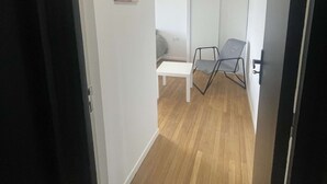 Un pasillo con una cama, una silla, una mesa y un cuadro en la pared.