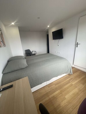 Ein modernes Schlafzimmer mit einem Bett, einem Schreibtisch, einem Stuhl, einem an der Wand montierten Fernseher und einer Tür.