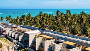 A hotel with multiple floors, a rooftop terrace, and a view of the ocean and palm trees.